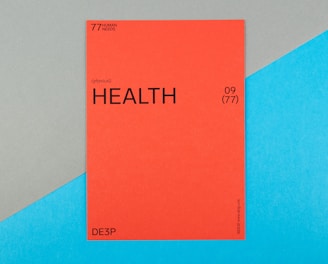 A vibrant red card with the word 'HEALTH' prominently displayed in black text, accompanied by smaller text indicating the number 09 (77) and phrases such as '77 HUMAN NEEDS' and '(physical)' at the top. The background consists of intersecting areas of blue and gray-green color.