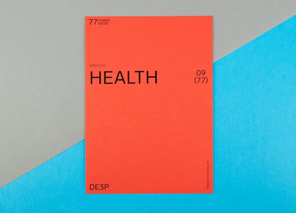 A vibrant red card with the word 'HEALTH' prominently displayed in black text, accompanied by smaller text indicating the number 09 (77) and phrases such as '77 HUMAN NEEDS' and '(physical)' at the top. The background consists of intersecting areas of blue and gray-green color.